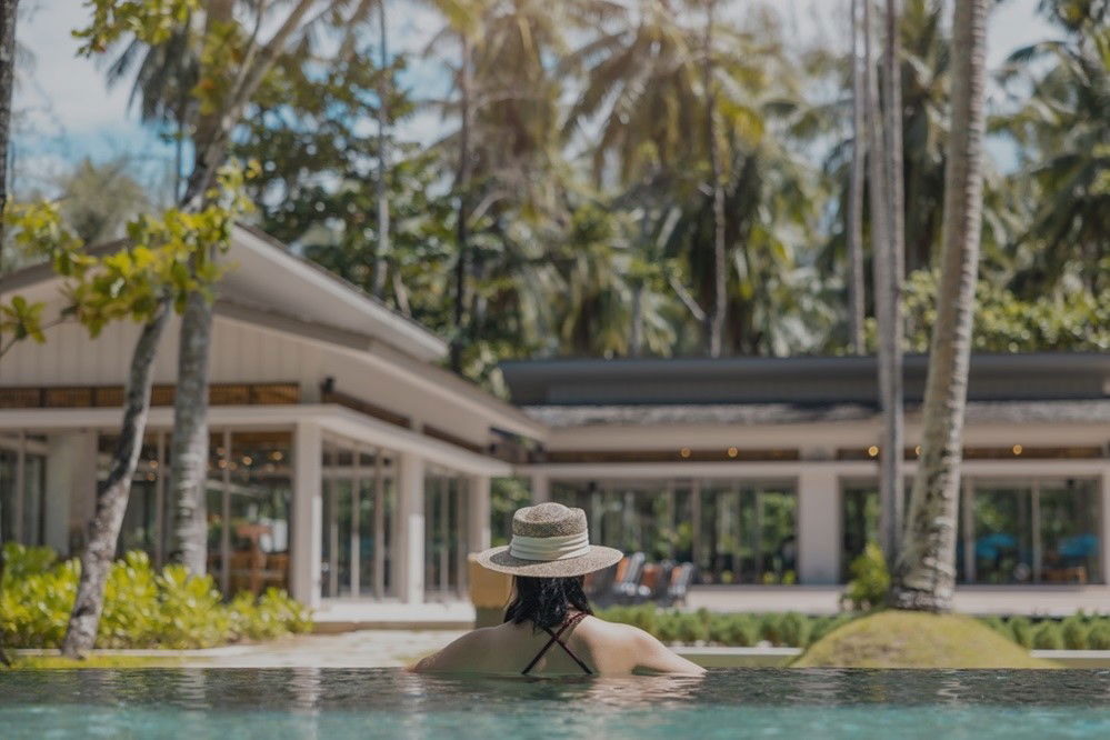 Frau im Pool vor Haus und Palmen