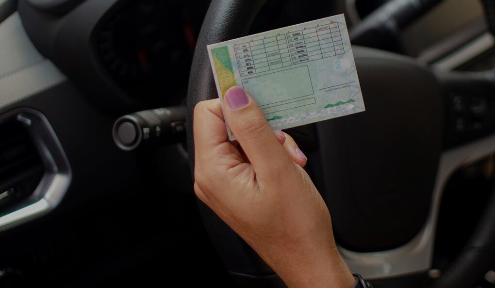 Frau sitzt im Auto und hält Führerschein in der Hand