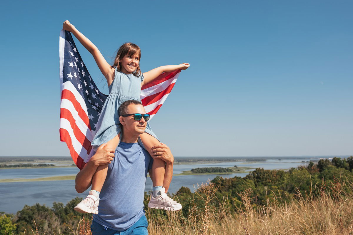 A man with daughter on his shoulders with US flag