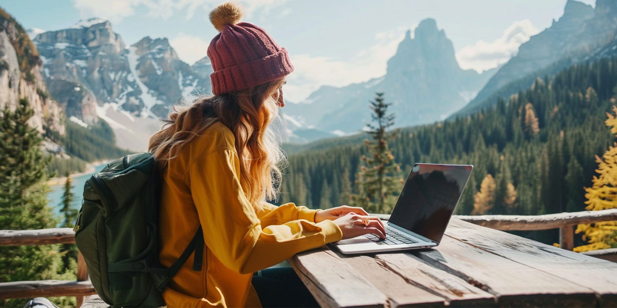 Frau sitzt mit Laptop am Tisch mit Bergen im Hintergrund