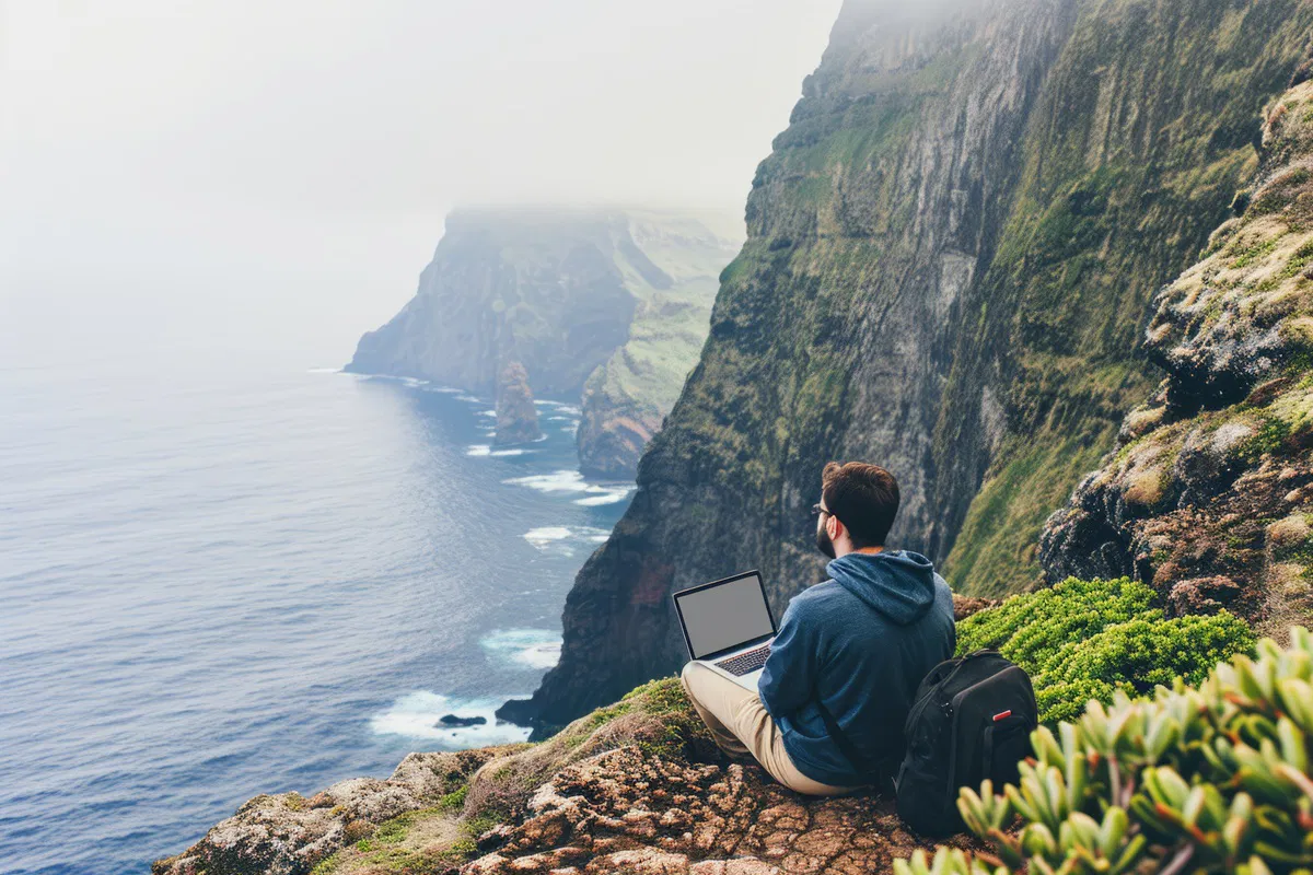 Man sitting on a cliff with his laptop looking over the ocean