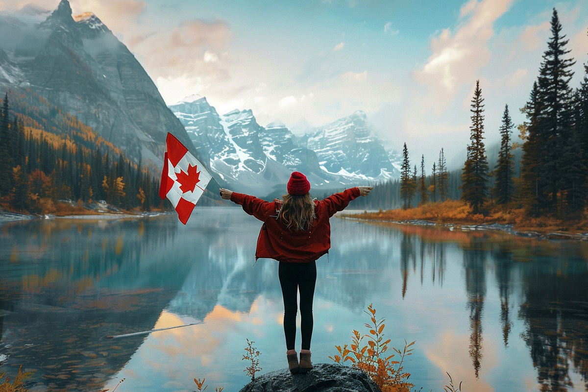 Woman standing in front of a lake holding a Canadian flag with the mountains and woods in the background