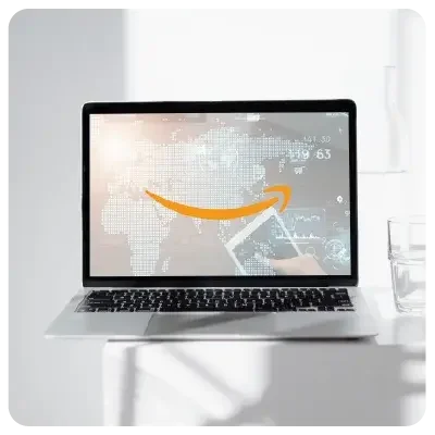 A light-coloured laptop stands open in an all-white room. The Amazon logo is clearly visible on the monitor.