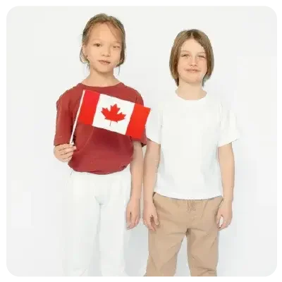A boy and a girl stand in front of a white wall. The girl is holding a Canada flag.