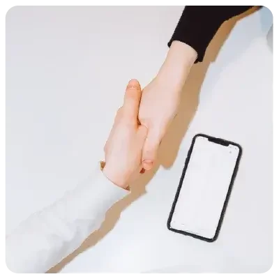 Two people shake hands over a white surface.