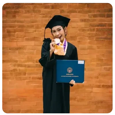 Una graduada universitaria con bata negra y sombrero académico sostiene con orgullo su certificado de graduación en la foto y muerde juguetonamente su medalla de graduación.