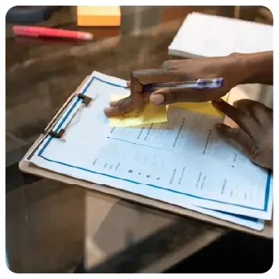 Vista de un portapapeles con un cuestionario. Una mano pega un post-it amarillo al trozo de papel.