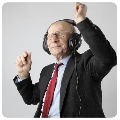 Rentner mit Brille und in schwarzem Anzug und roter Krawatte tanzt zu Musik, die aus den Headphones auf seinem Kopf zu kommen scheint.