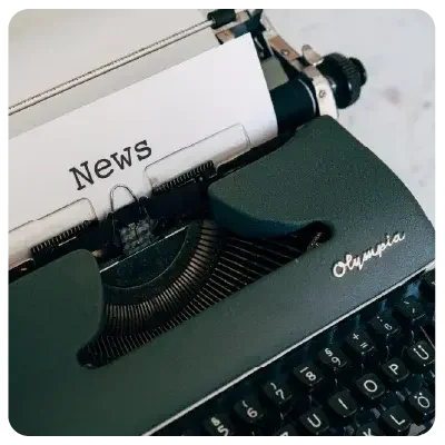 Vista de una máquina de escribir negra con una hoja de papel sujeta en ella, en la que está escrito "News" en el centro.
