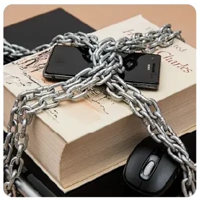 Ein Handy liegt auf einem dicken Buch. Beide sind mit dicken Metallketten umschlossen.