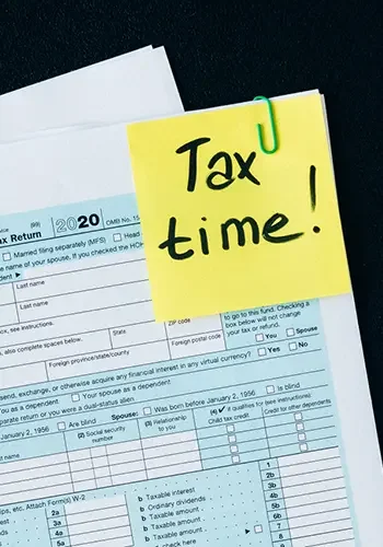 Auf Steuererunterlagen klebt ein Post-It mit dem Text "Tax time".