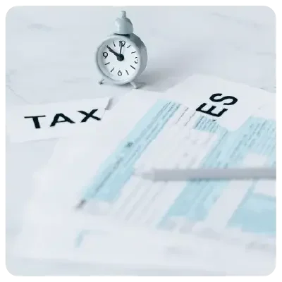 Tax documents lie on a white table together with a miniature alarm clock.