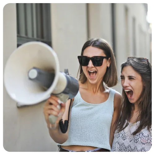 Zwei junge Frauen schreien durch ein Megaphon.