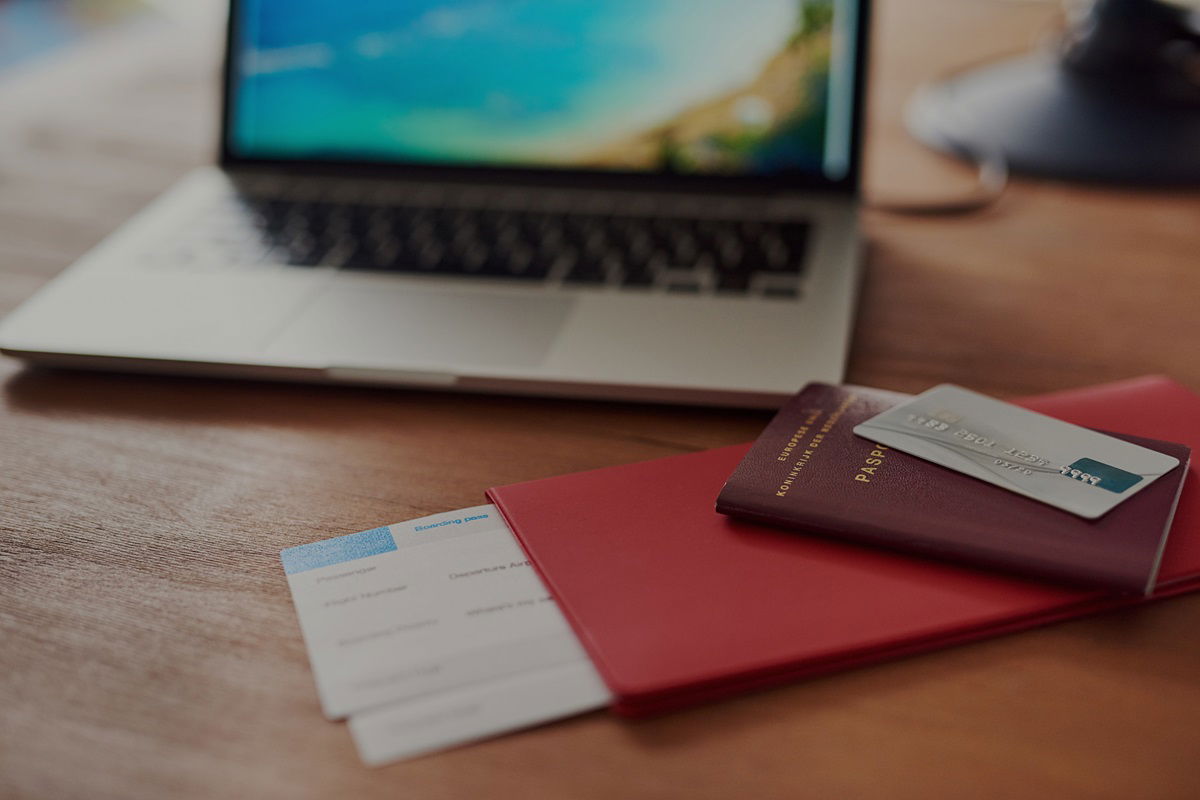 Passport and flight tickets lying on a table with a laptop in the background