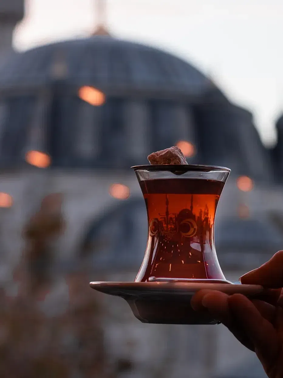 Person hält türkischen Tee vor einer Moschee