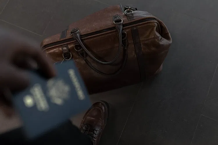 Someone standing in front of his suitcase with passport in hands