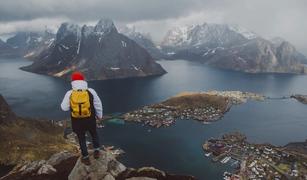 Mann steht in Norwegen auf einem Berg und blickt auf Fjorde