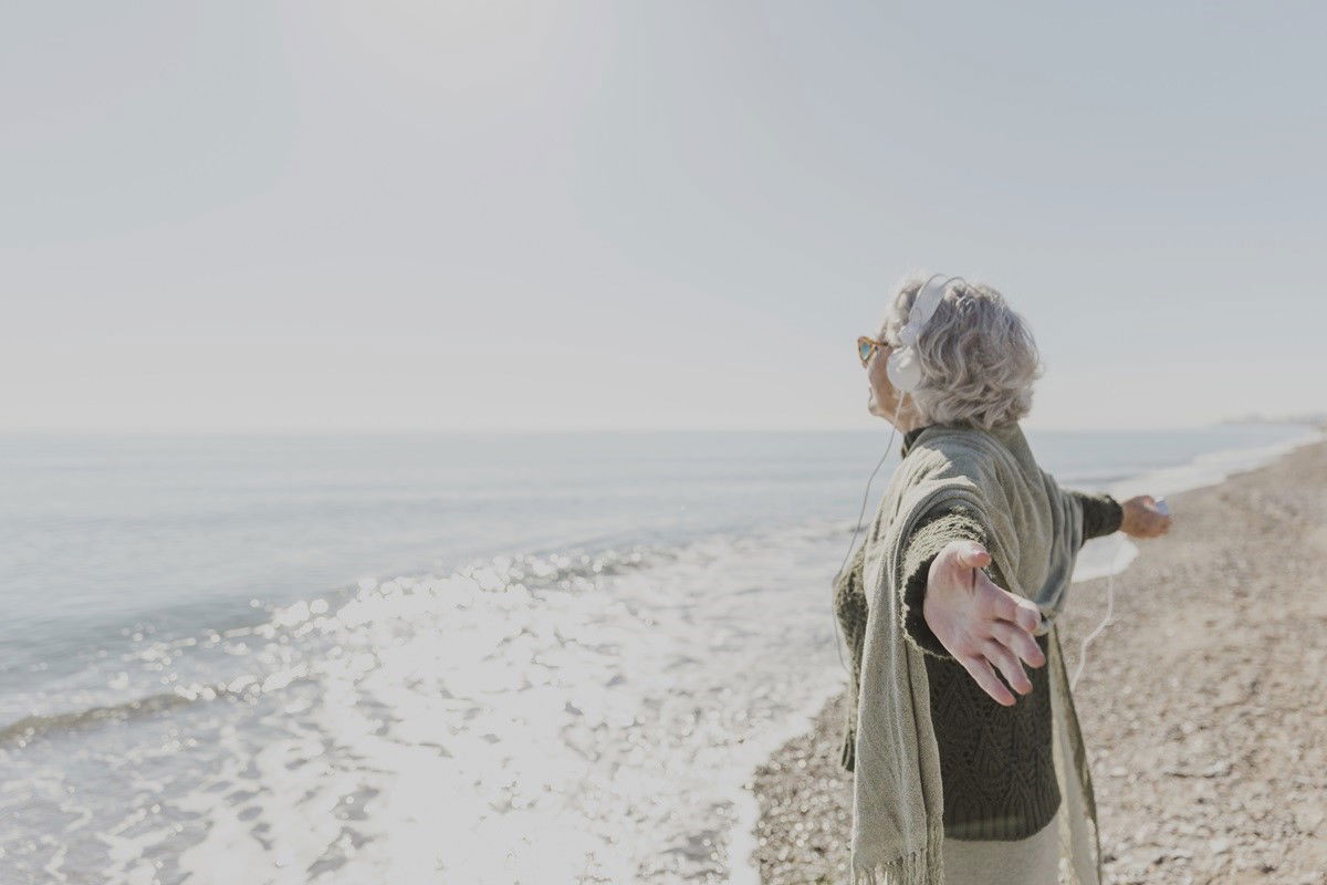 Frau steht am Meer und streckt Arme aus