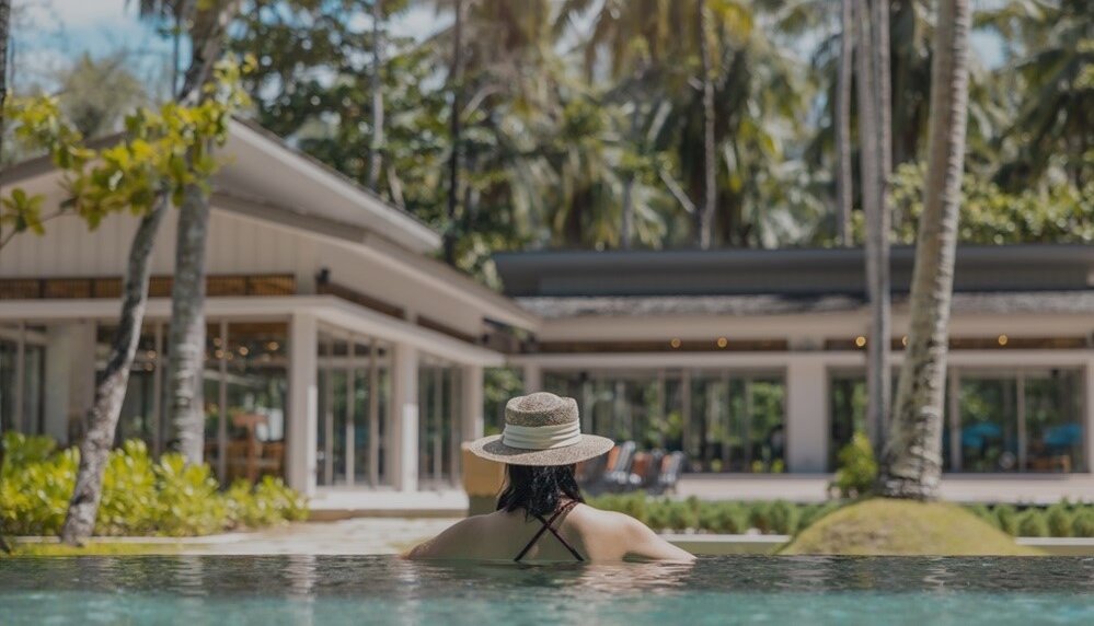 Woman in pool in front of house and palm trees 