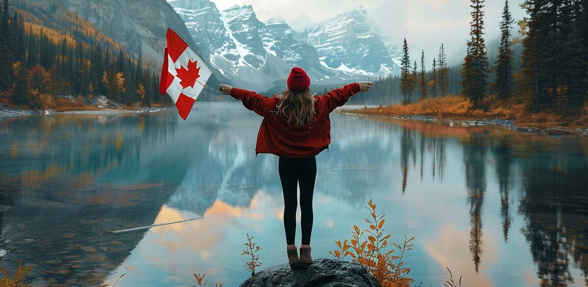 Woman standing in front of a lake with mountains in the background holding a Canadian flag