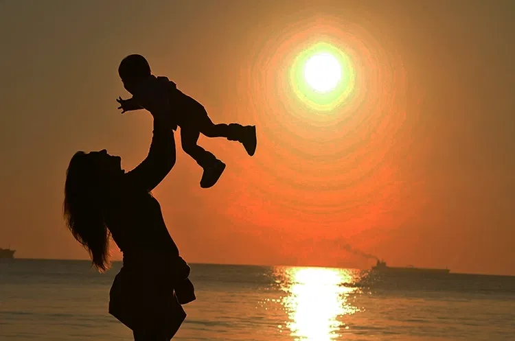 Woman holds Child up high during sunset