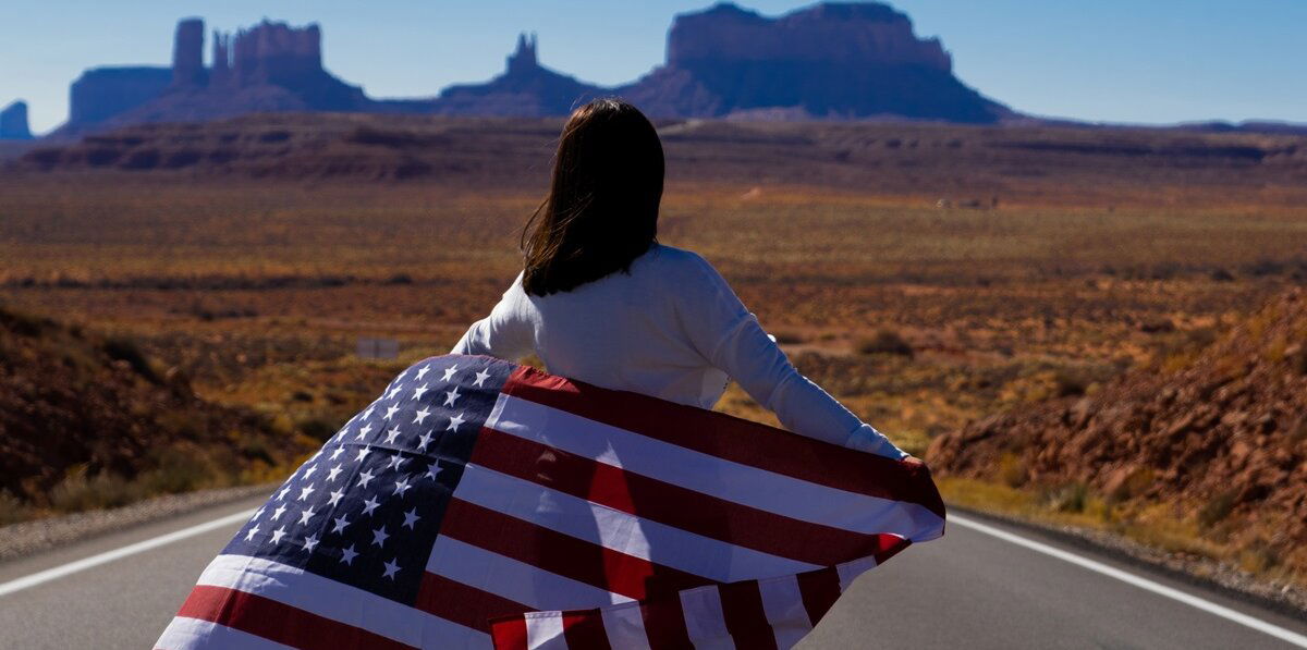 Woman standing on a highway in the desert of the USA with an US flag