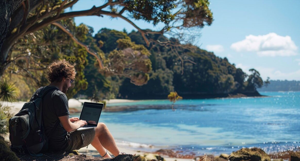 Work and Travel Australien: Mann sitzt mit Laptop am Strand