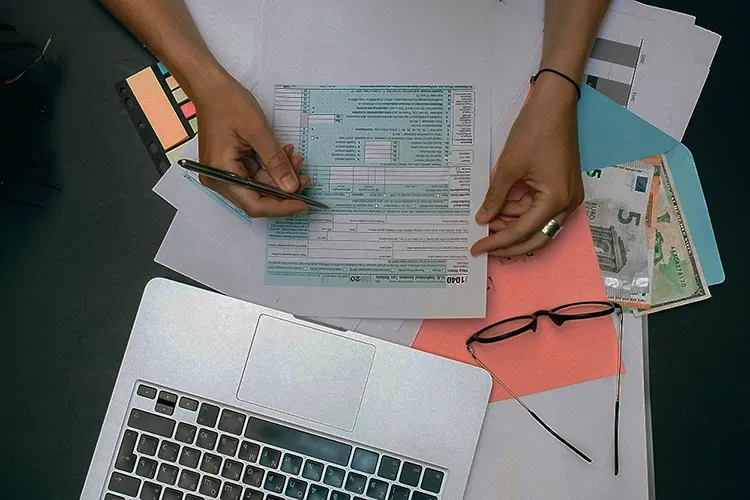 Laptop and bank notes on a table and someone holding a form