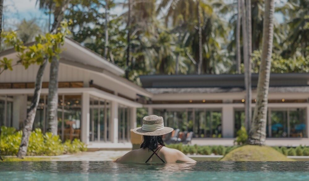 Frau im Pool vor Haus und Palmen